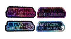 Four holographic stickers with the text 'BE PEACFUL NOT HARMLESS' arranged in a 2x2 grid on a solid black background.