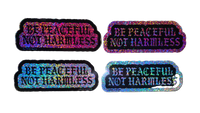 Four holographic stickers with the text 'BE PEACFUL NOT HARMLESS' arranged in a 2x2 grid on a solid black background.
