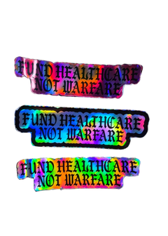 Three identical rectangular stickers with a holographic rainbow sheen and black text reading 'FUND HEALTHCARE NOT WARFARE' on a plain white background.