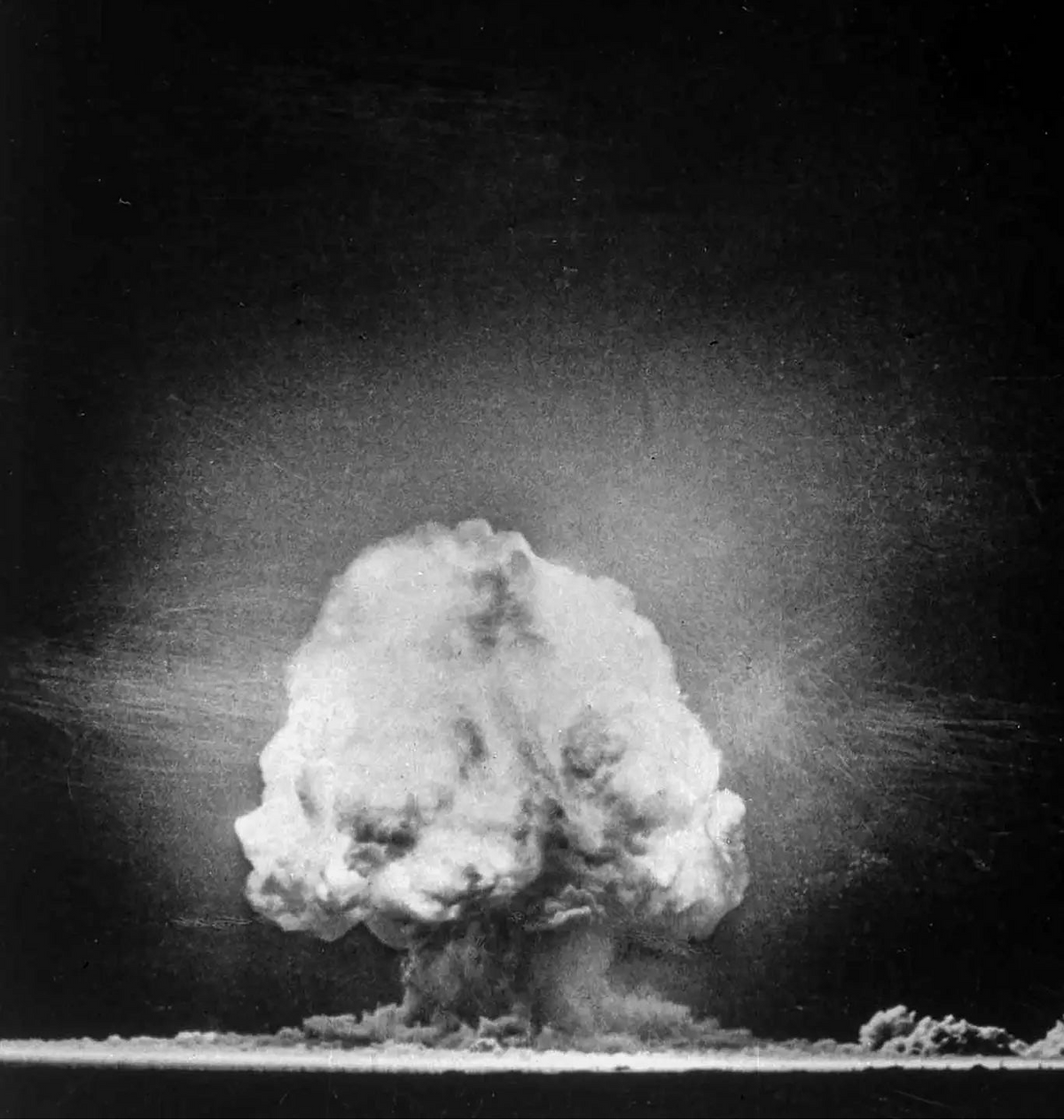 Black and white photograph of a large mushroom cloud explosion rising from a surface against a dark sky.