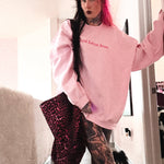 Person wearing a pink sweatshirt with text, holding a leopard print bag indoors.