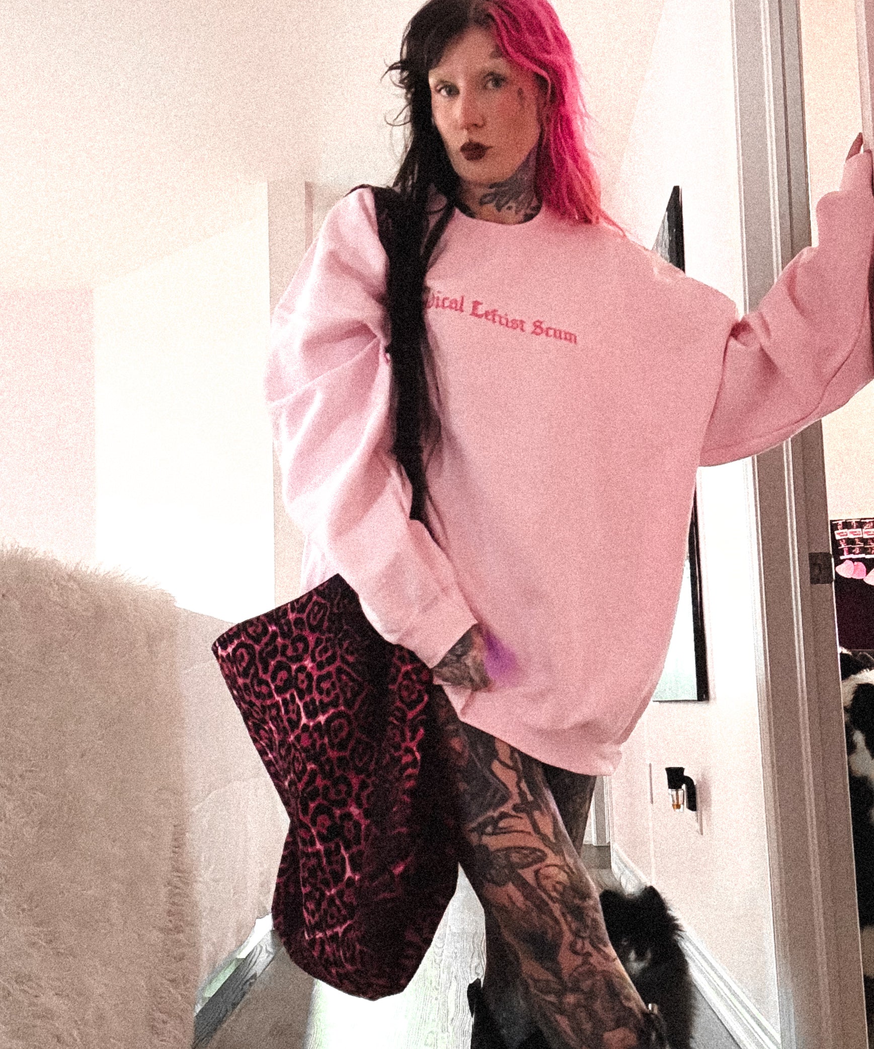 Person wearing a pink sweatshirt with text, holding a leopard print bag indoors.