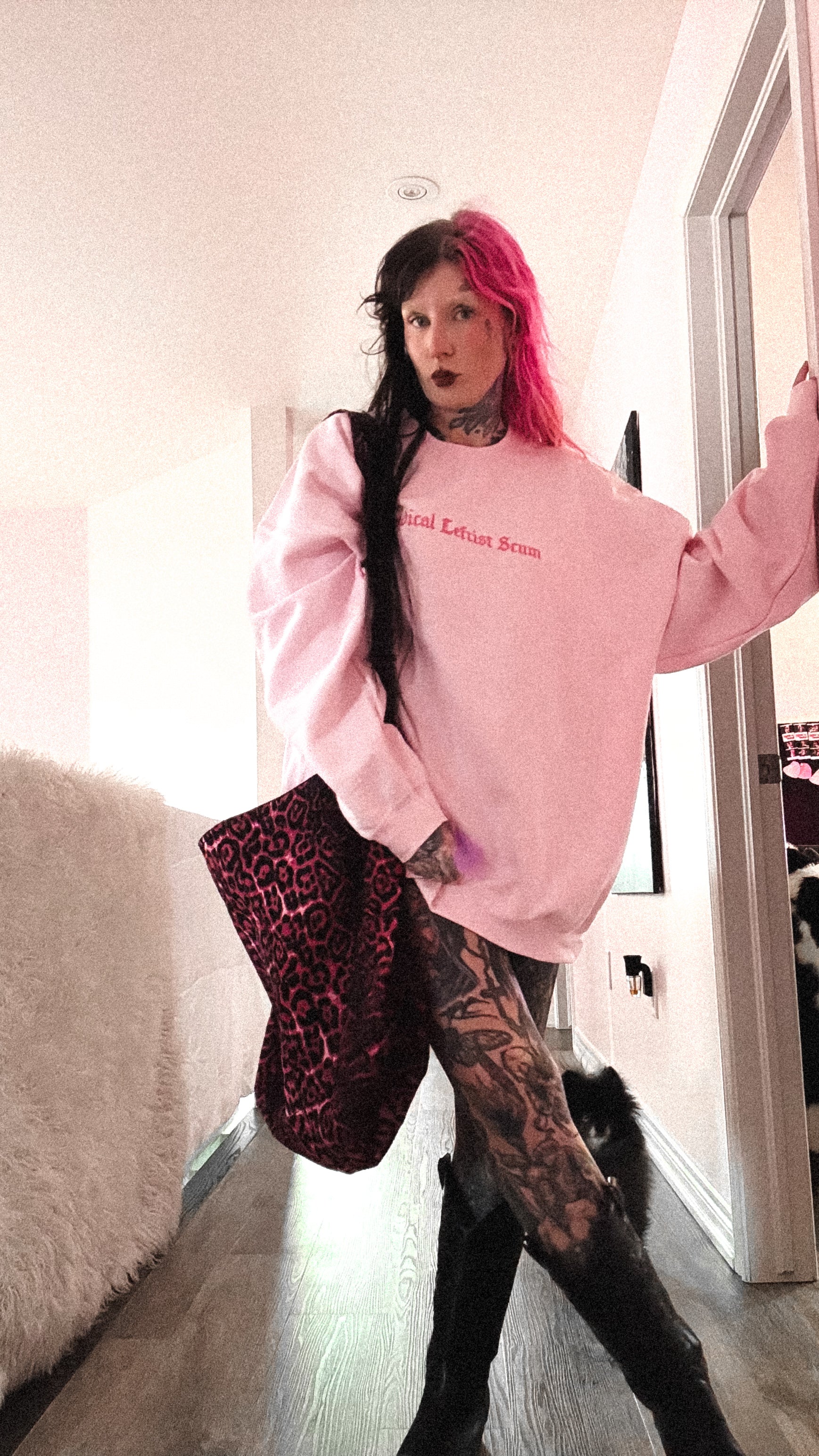 Person wearing a pink sweatshirt with text, holding a leopard print bag indoors.
