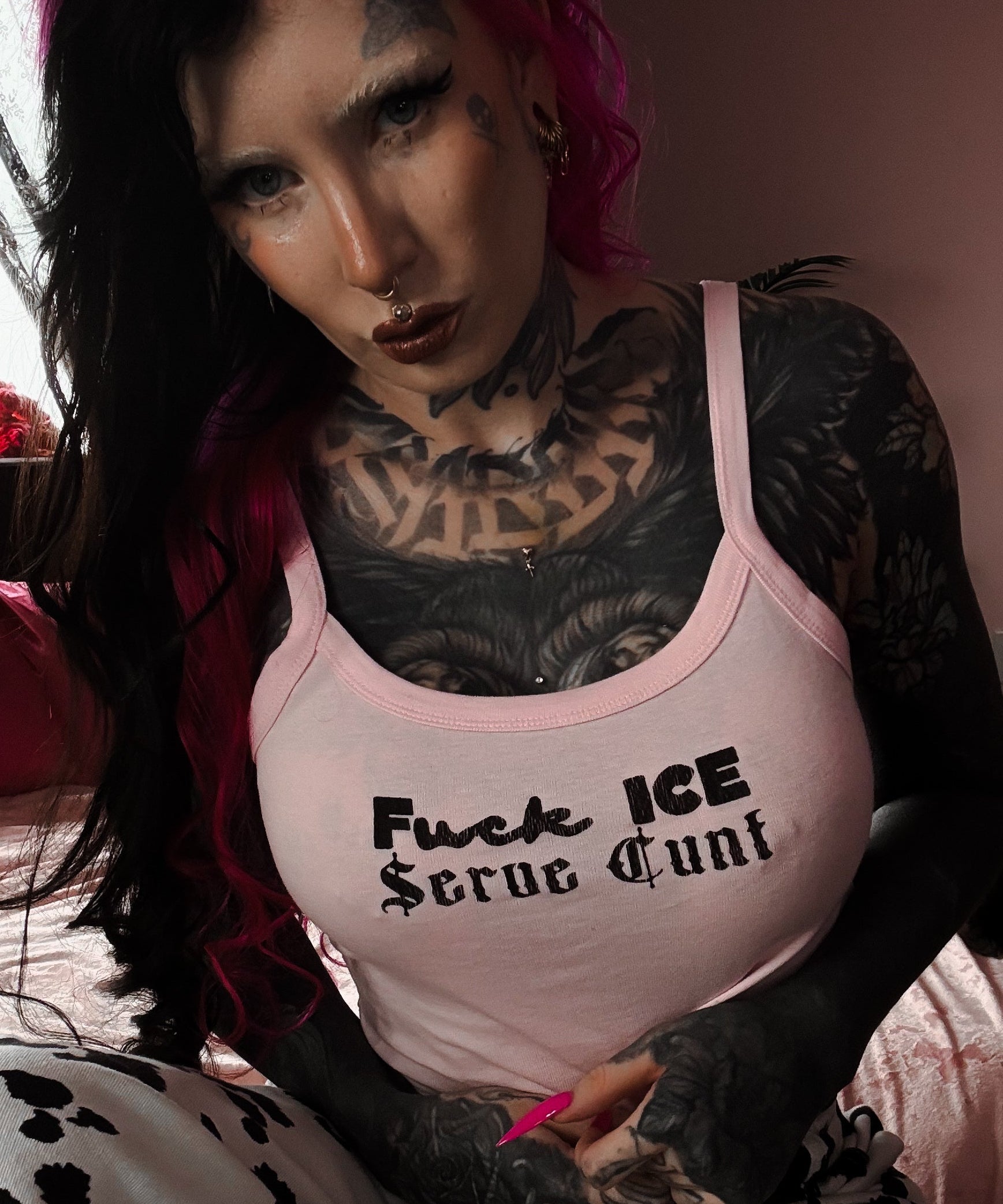 Person with tattoos and pink hair wearing a tank top with text.