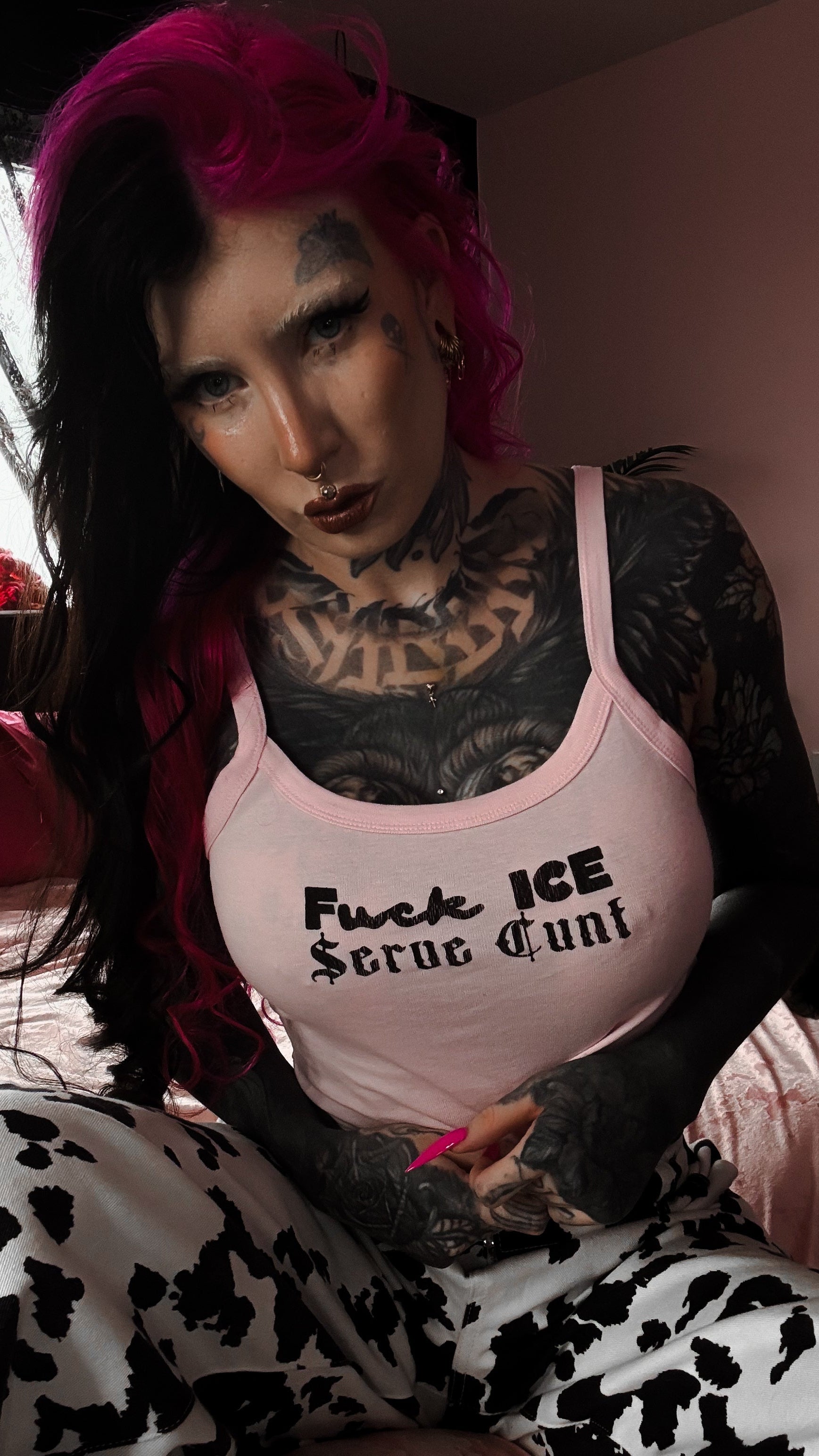 Person with tattoos and pink hair wearing a tank top with text.