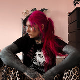 Person with pink hair and tattoos sitting on a chair against a pink wall.