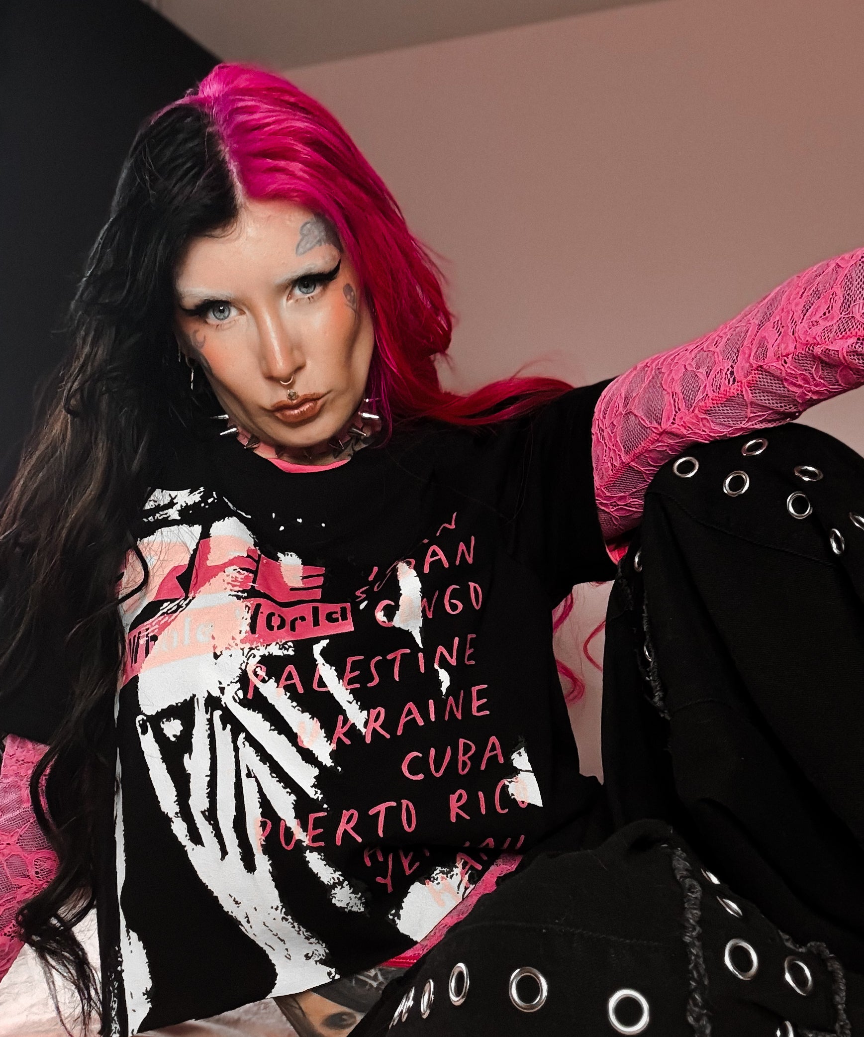 Person with pink hair and black outfit sitting on a bed