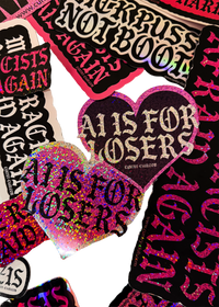 Heart-shaped "AI Is for Losers" glitter stickers in pink and black on a pile of other Cuntry Club stickers