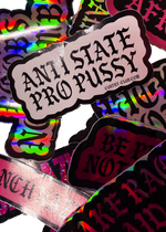 Close-up of a white Anti State Pro Pussy sticker resting on holographic stickers