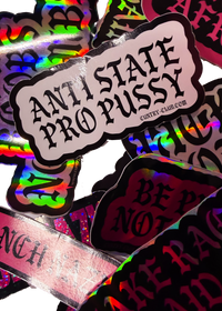 Close-up of a white Anti State Pro Pussy sticker resting on holographic stickers