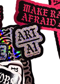 Silver glitter "Art Over AI" sticker, Art above a line and AI below, on a pile of Cuntry Club stickers