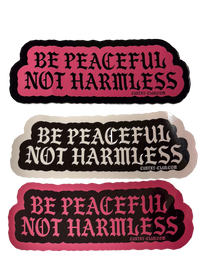 Three scalloped bumper stickers with the text 'BE PEACFUL NOT HARMLESS' in black gothic lettering. The top and bottom stickers have a pink background, and the middle sticker has a light beige background.