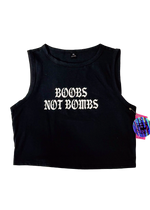 Black cropped tank top laid flat with "Boobs Not Bombs" in white gothic letters and a holographic hangtag