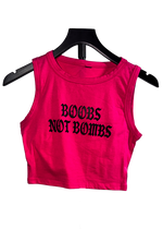 A bright pink sleeveless crop top with the text 'BOOBS NOT BOMBS' printed in black gothic font, displayed on a black hanger against a white background.
