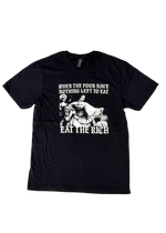 Black t-shirt laid flat with a black and white classical painting of women at a feast and gothic text reading "When the poor have nothing left to eat, eat the rich"
