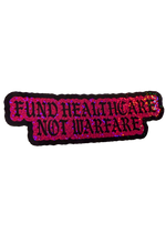 Pink glitter Fund Healthcare Not Warfare sticker with black gothic lettering