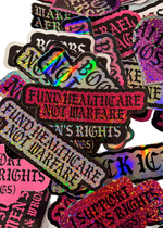"Fund Healthcare Not Warfare" stickers in pink and white on a pile of Cuntry Club stickers