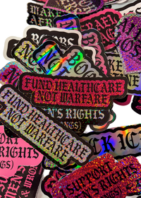 "Fund Healthcare Not Warfare" stickers in pink and white on a pile of Cuntry Club stickers