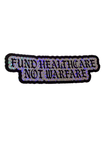 Silver glitter Fund Healthcare Not Warfare sticker with black gothic lettering