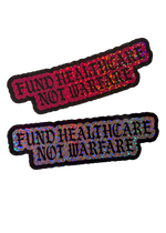 Two Fund Healthcare Not Warfare glitter stickers, one pink and one silver