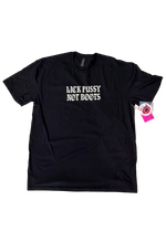Black t-shirt laid flat with "Lick Pussy Not Boots" in small white gothic letters on the chest and a pink hangtag pinned to the sleeve