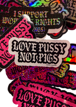 White "Love Pussy Not Pigs" sticker with black gothic lettering on a pile of pink, glitter and holographic Cuntry Club stickers