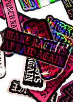 Make Racists Afraid Again sticker with pink holographic lettering on a pile of stickers
