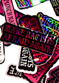 Make Racists Afraid Again sticker with pink holographic lettering on a pile of stickers