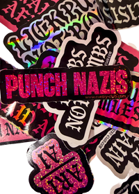 Black Punch Nazis sticker with pink glitter lettering on a pile of stickers